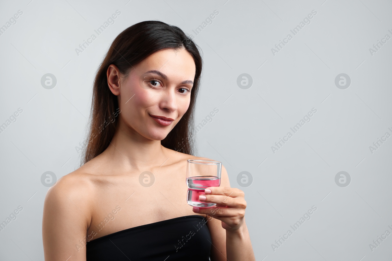 Photo of Young woman with cap of mouthwash on grey background, space for text. Oral hygiene