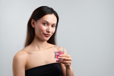 Photo of Young woman with cap of mouthwash on grey background, space for text. Oral hygiene