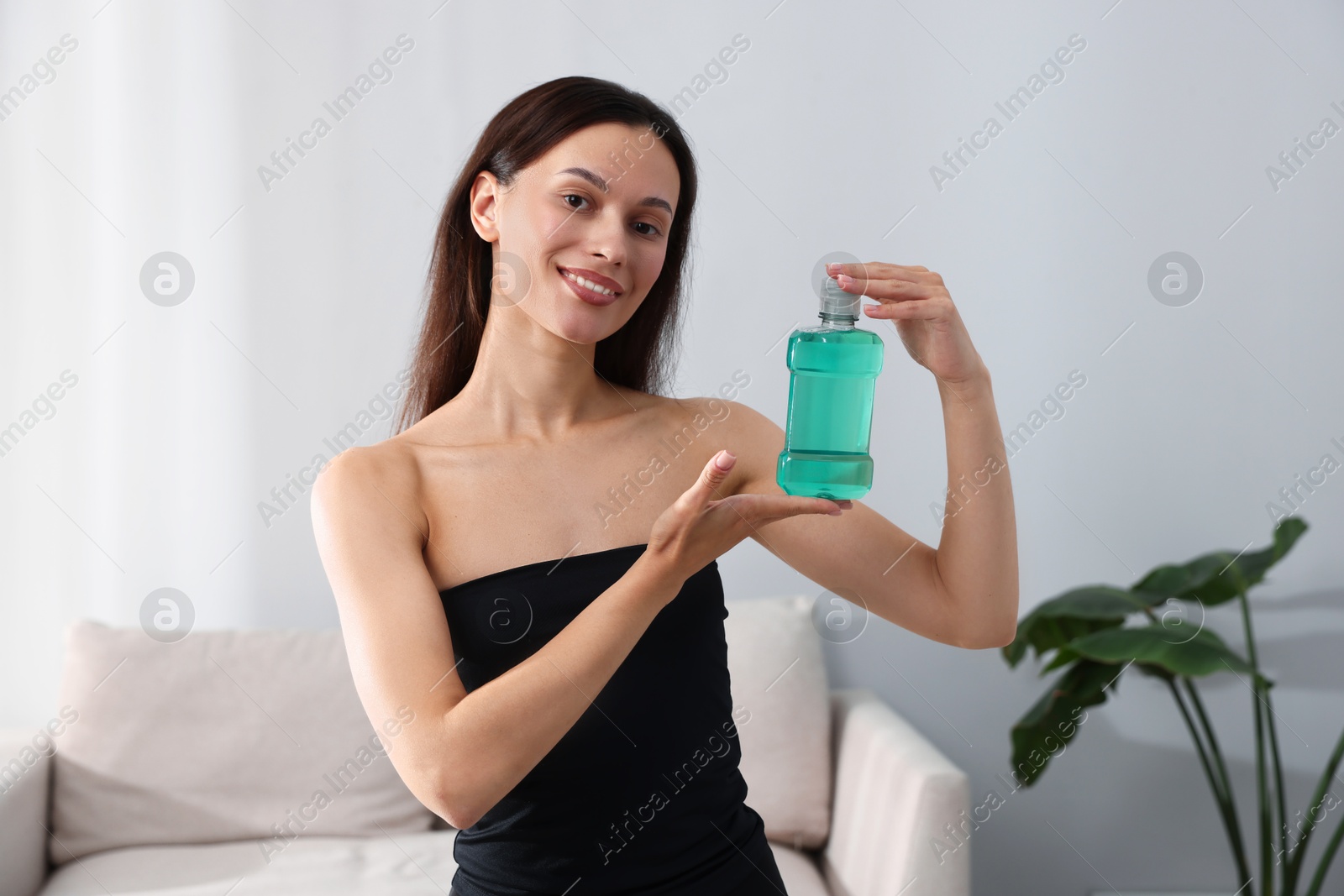Photo of Smiling young woman with bottle of mouthwash at home. Oral hygiene