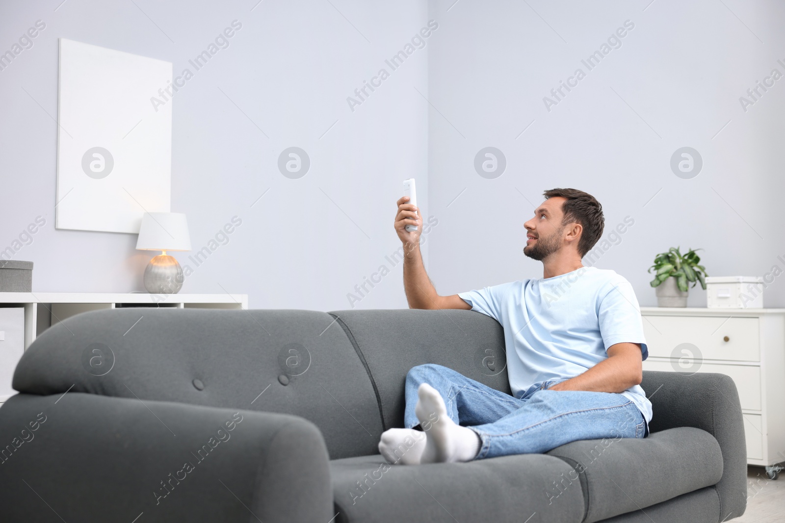 Man using remote to control air conditioner on sofa at home. Space for text Photo of Man using remote to control air conditioner on sofa at home. Space for text