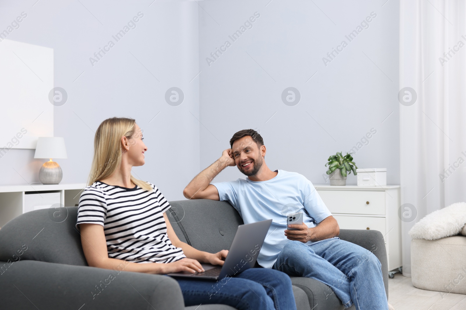 Photo of Happy couple with devices spending time together on sofa at home