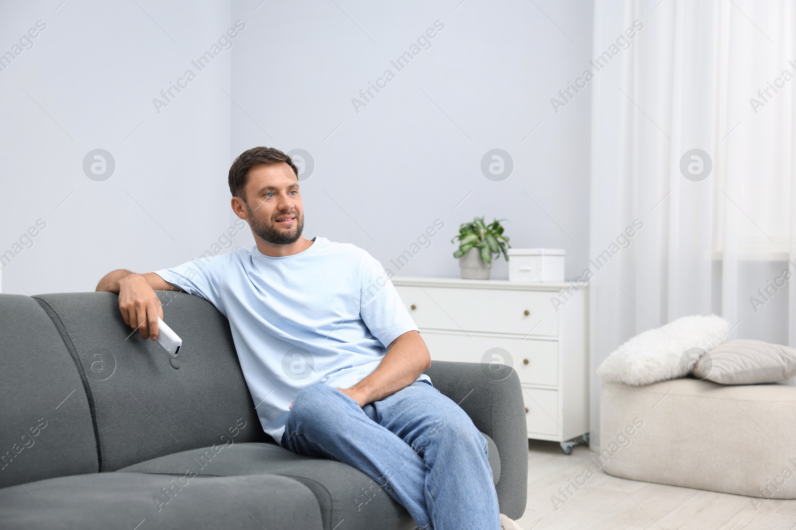 Photo of Man with air conditioner remote control on sofa at home. Space for text