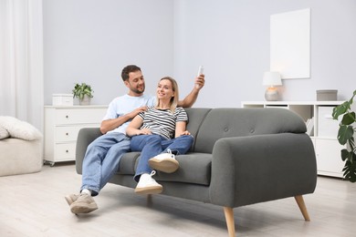 Photo of Couple using remote to control air conditioner on sofa at home