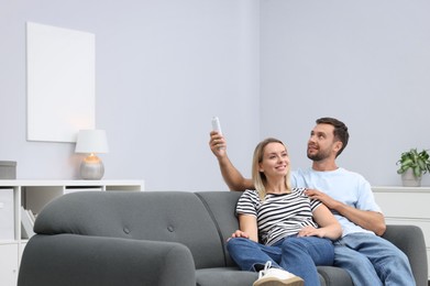 Photo of Couple using remote to control air conditioner on sofa at home. Space for text