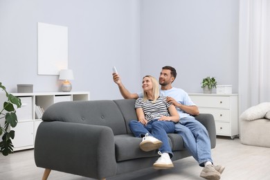 Photo of Couple using remote to control air conditioner on sofa at home