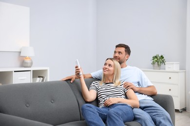 Photo of Couple using remote to control air conditioner on sofa at home. Space for text