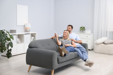 Photo of Couple using remote to control air conditioner on sofa at home. Space for text