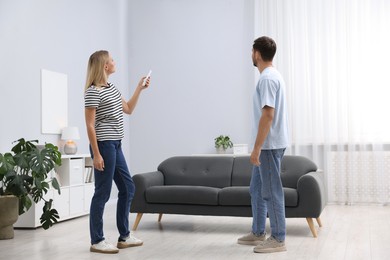 Photo of Couple using remote to control air conditioner at home