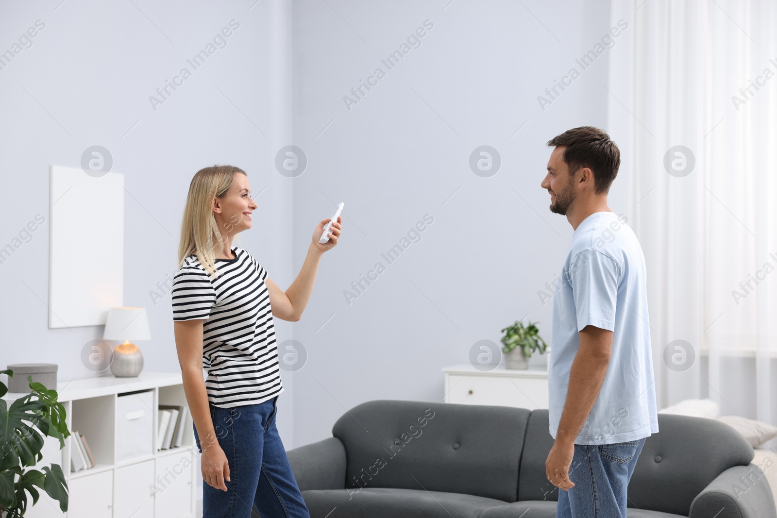 Photo of Couple using remote to control air conditioner at home