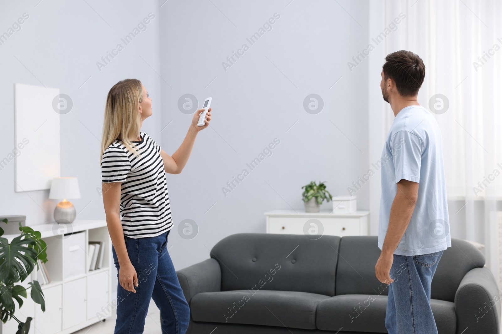 Couple using remote to control air conditioner at home Photo of Couple using remote to control air conditioner at home