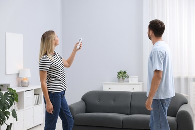 Photo of Couple using remote to control air conditioner at home