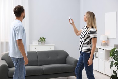 Photo of Couple using remote to control air conditioner at home