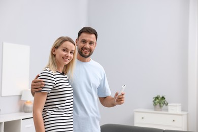 Photo of Couple using remote to control air conditioner at home. Space for text