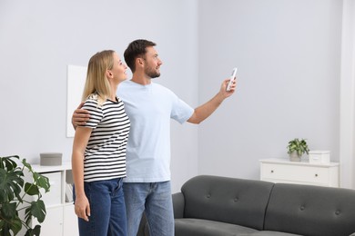 Photo of Couple using remote to control air conditioner at home