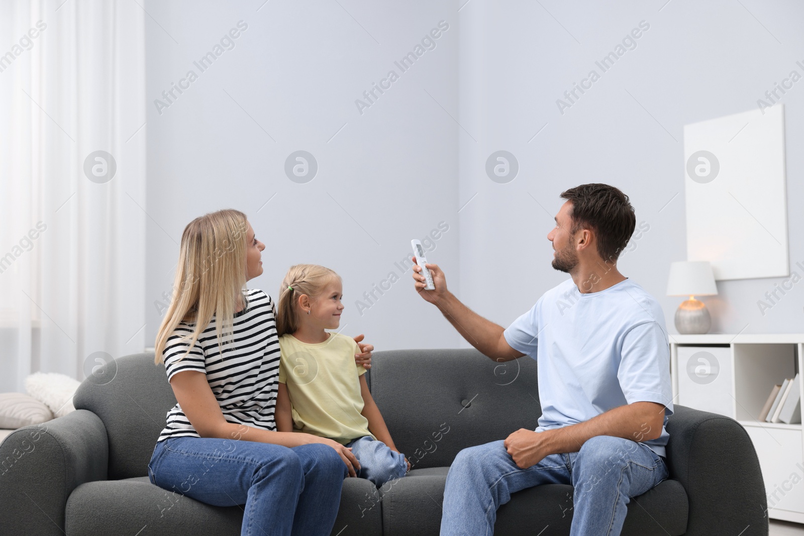 Photo of Happy family using remote to control air conditioner on sofa at home