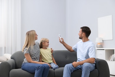 Photo of Happy family using remote to control air conditioner on sofa at home