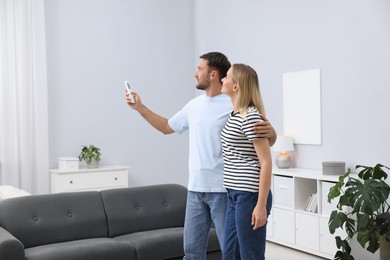 Photo of Couple using remote to control air conditioner at home