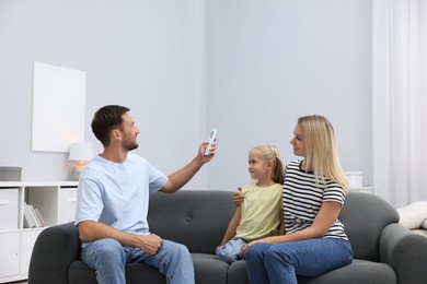 Photo of Happy family using remote to control air conditioner on sofa at home