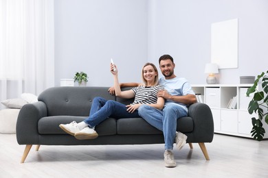 Photo of Couple using remote to control air conditioner on sofa at home