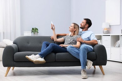 Photo of Couple using remote to control air conditioner on sofa at home