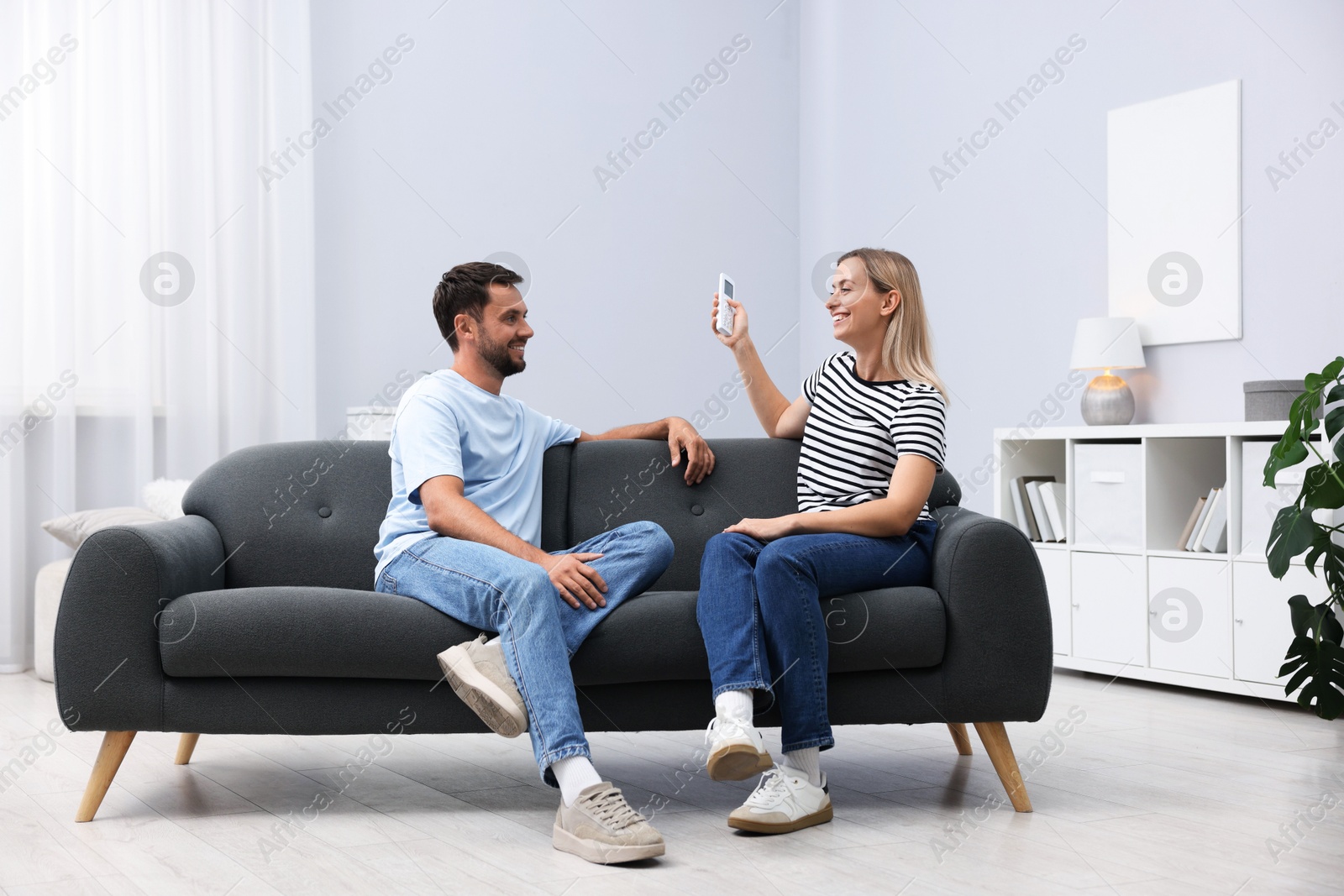 Photo of Couple using remote to control air conditioner on sofa at home