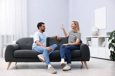 Photo of Couple using remote to control air conditioner on sofa at home