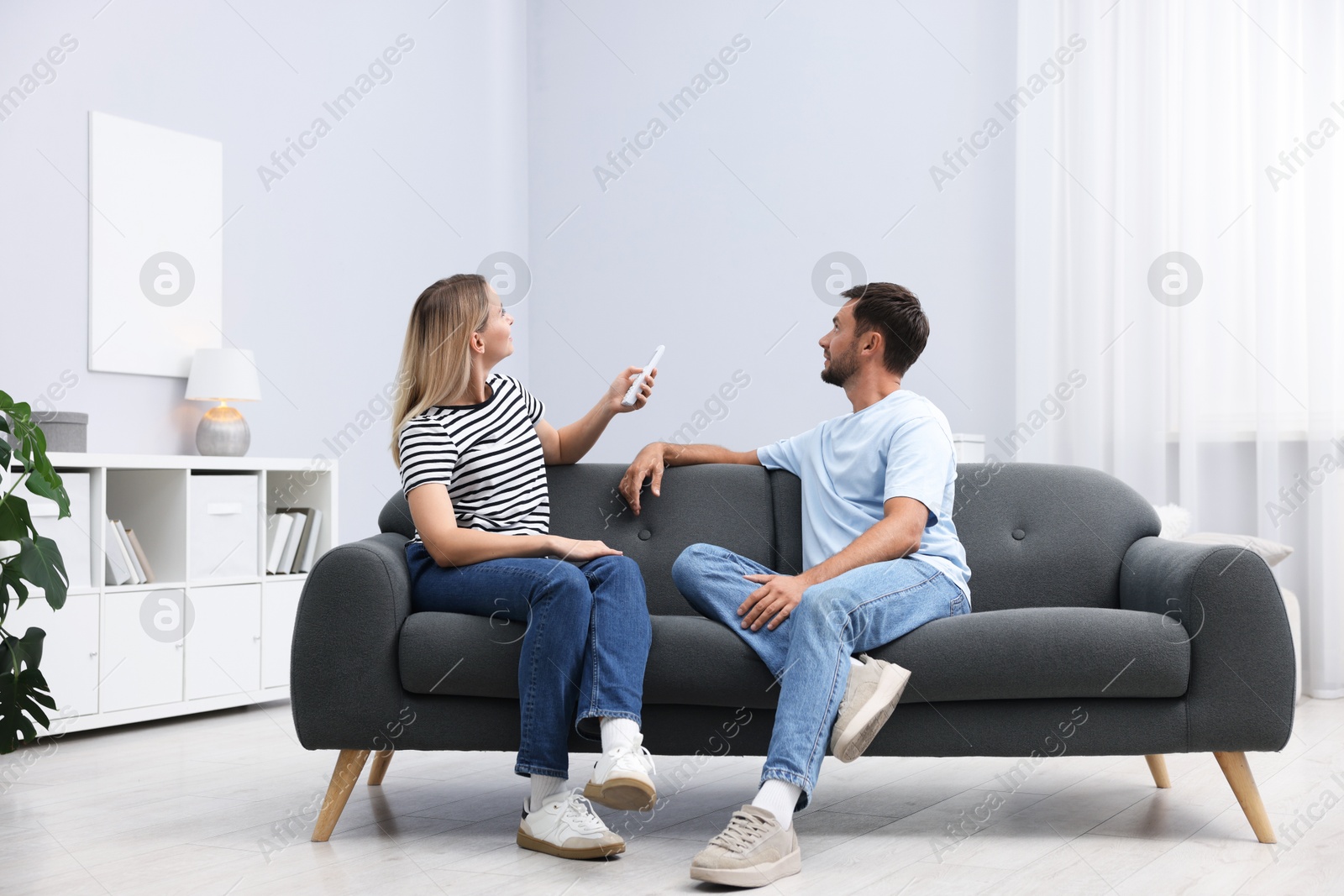 Photo of Couple using remote to control air conditioner on sofa at home
