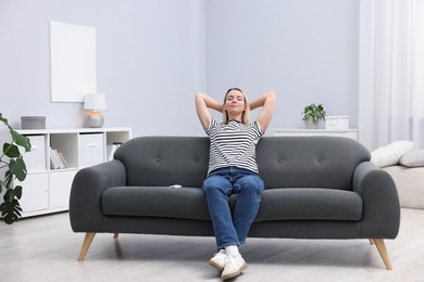 Photo of Woman with air conditioner remote control on sofa at home