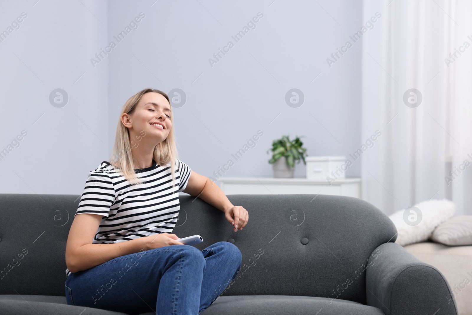 Photo of Woman with air conditioner remote control on sofa at home. Space for text
