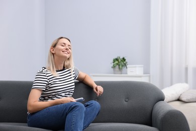 Photo of Woman with air conditioner remote control on sofa at home. Space for text