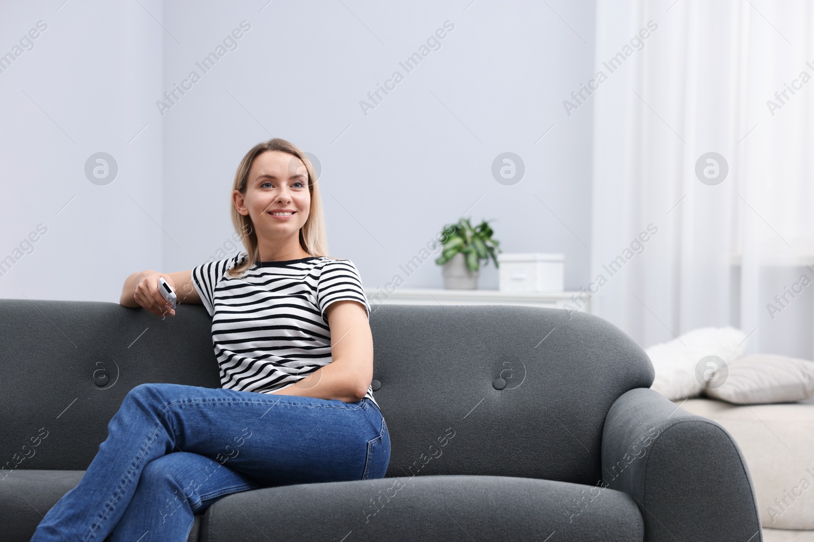 Photo of Woman with air conditioner remote control on sofa at home. Space for text