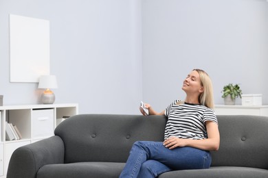 Photo of Woman with air conditioner remote control on sofa at home