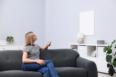 Photo of Woman using remote to control air conditioner on sofa at home. Space for text