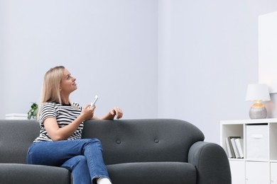 Photo of Woman using remote to control air conditioner on sofa at home. Space for text