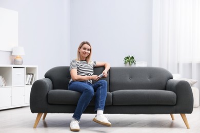 Photo of Woman with air conditioner remote control on sofa at home