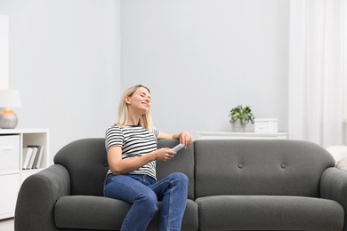 Photo of Woman with air conditioner remote control on sofa at home. Space for text