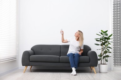 Photo of Woman using remote to control air conditioner on sofa at home. Space for text