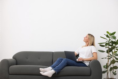 Photo of Woman with laptop on sofa at home. Space for text