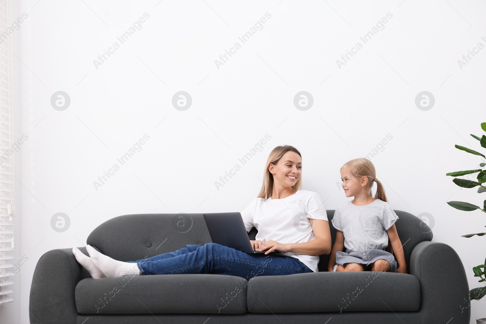Photo of Mother and daughter spending time together on sofa at home. Space for text
