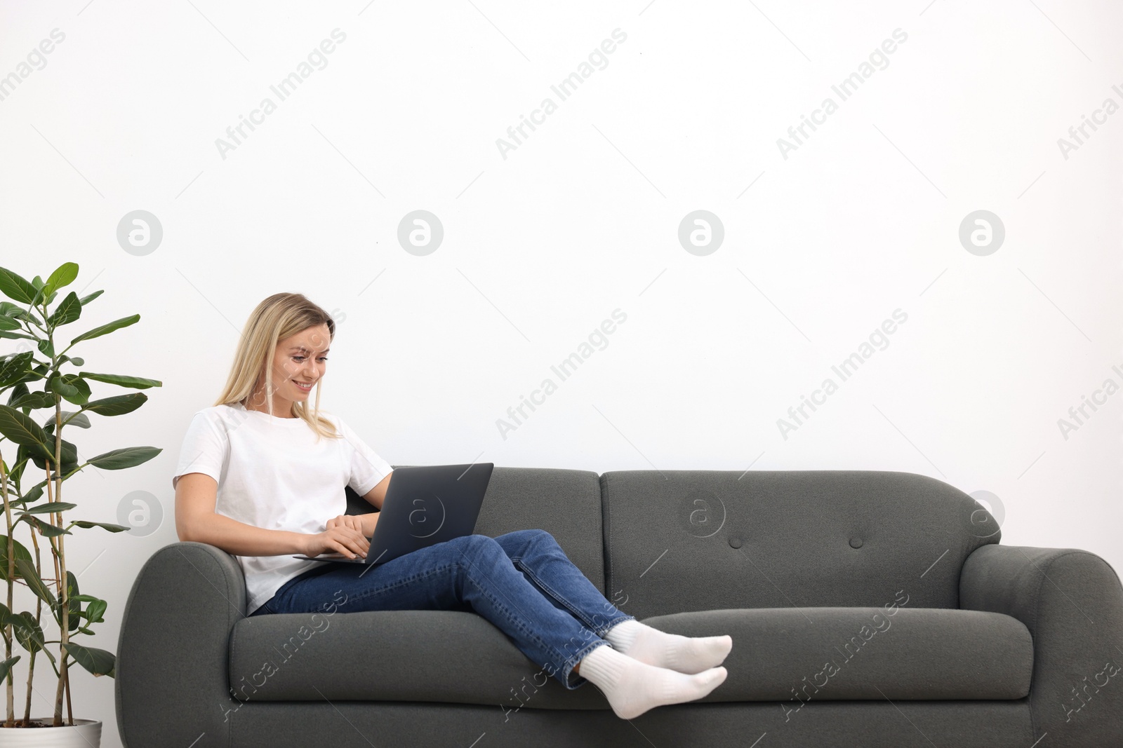 Photo of Woman with laptop on sofa at home. Space for text