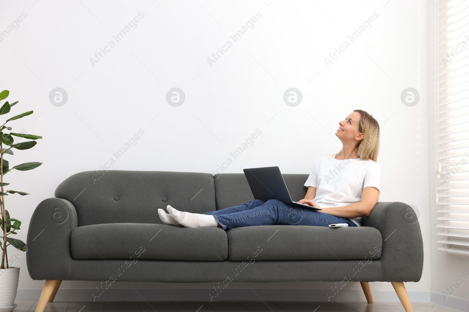 Woman with laptop on sofa at home. Space for text Photo of Woman with laptop on sofa at home. Space for text