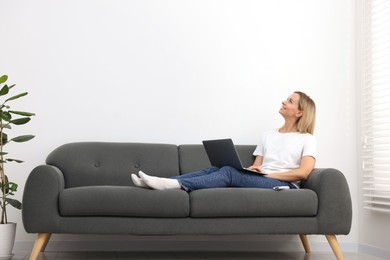 Photo of Woman with laptop on sofa at home. Space for text