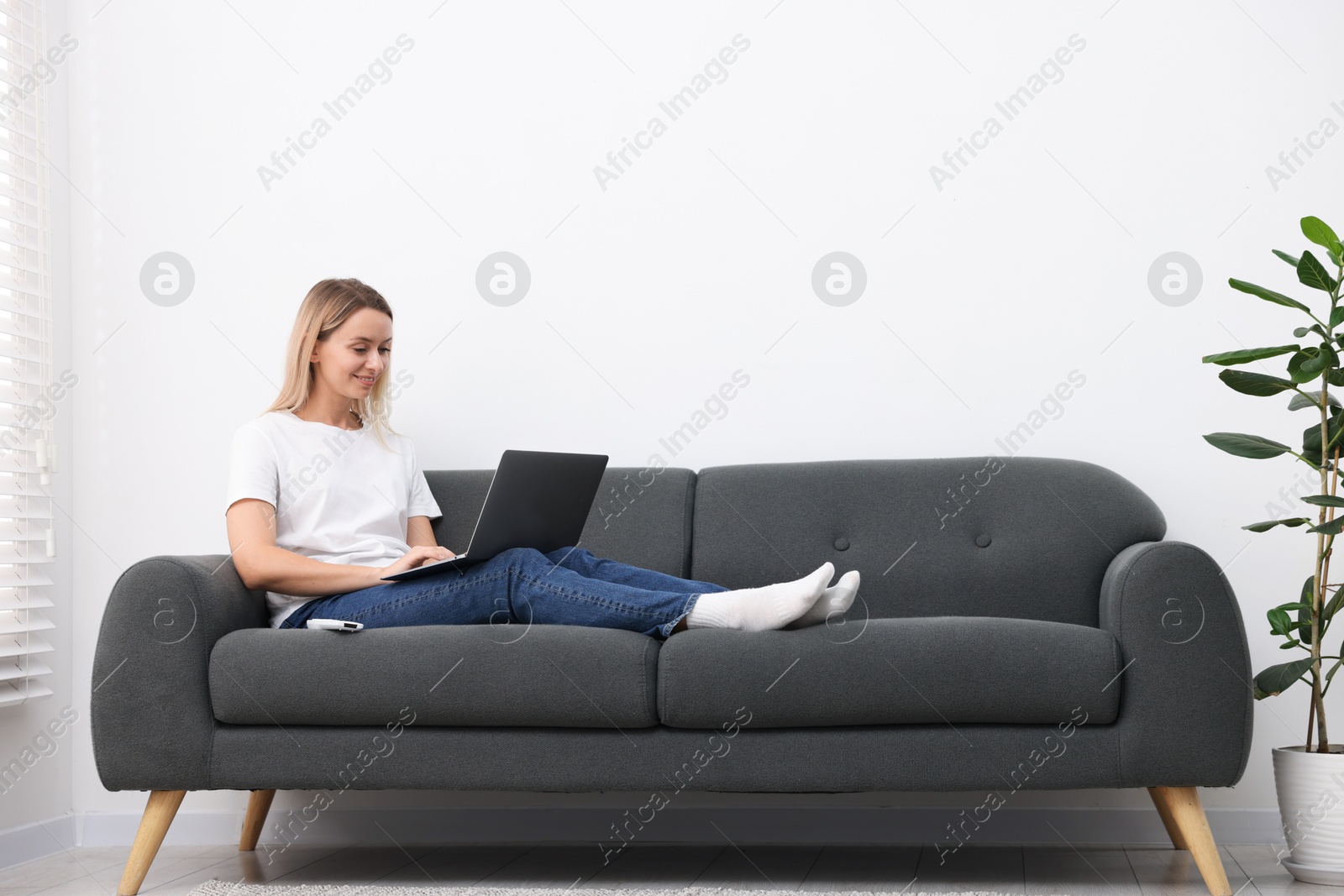 Photo of Woman with laptop on sofa at home. Space for text