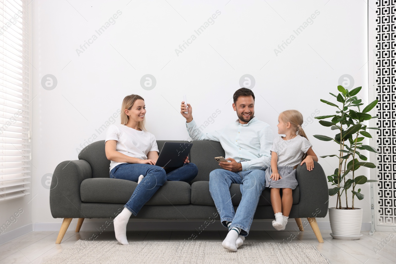 Photo of Happy family using remote to control air conditioner on sofa at home