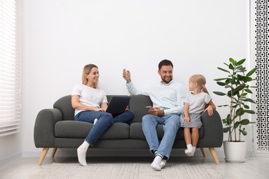 Photo of Happy family using remote to control air conditioner on sofa at home