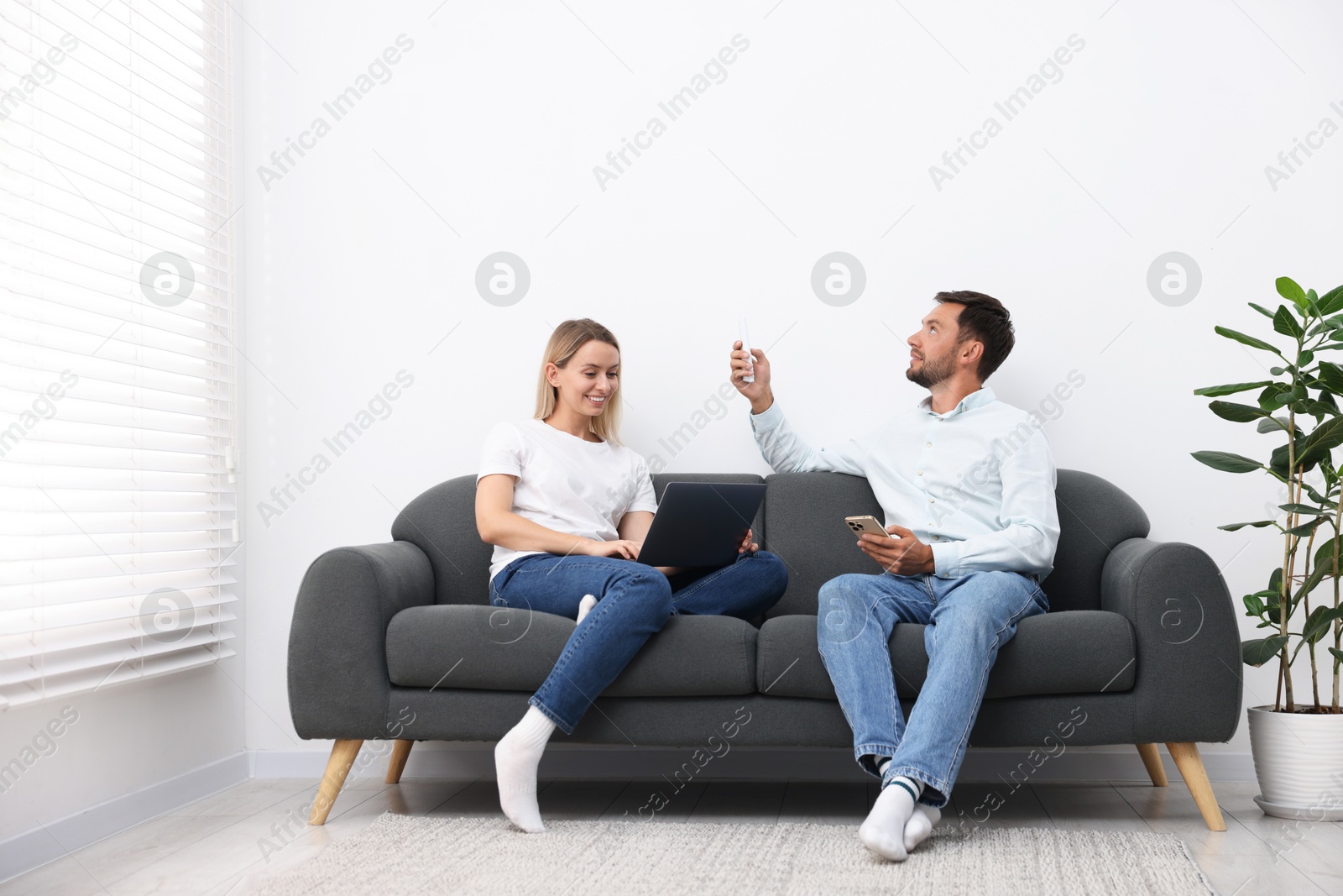 Photo of Couple using remote to control air conditioner on sofa at home