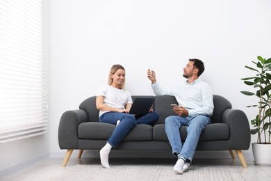 Photo of Couple using remote to control air conditioner on sofa at home