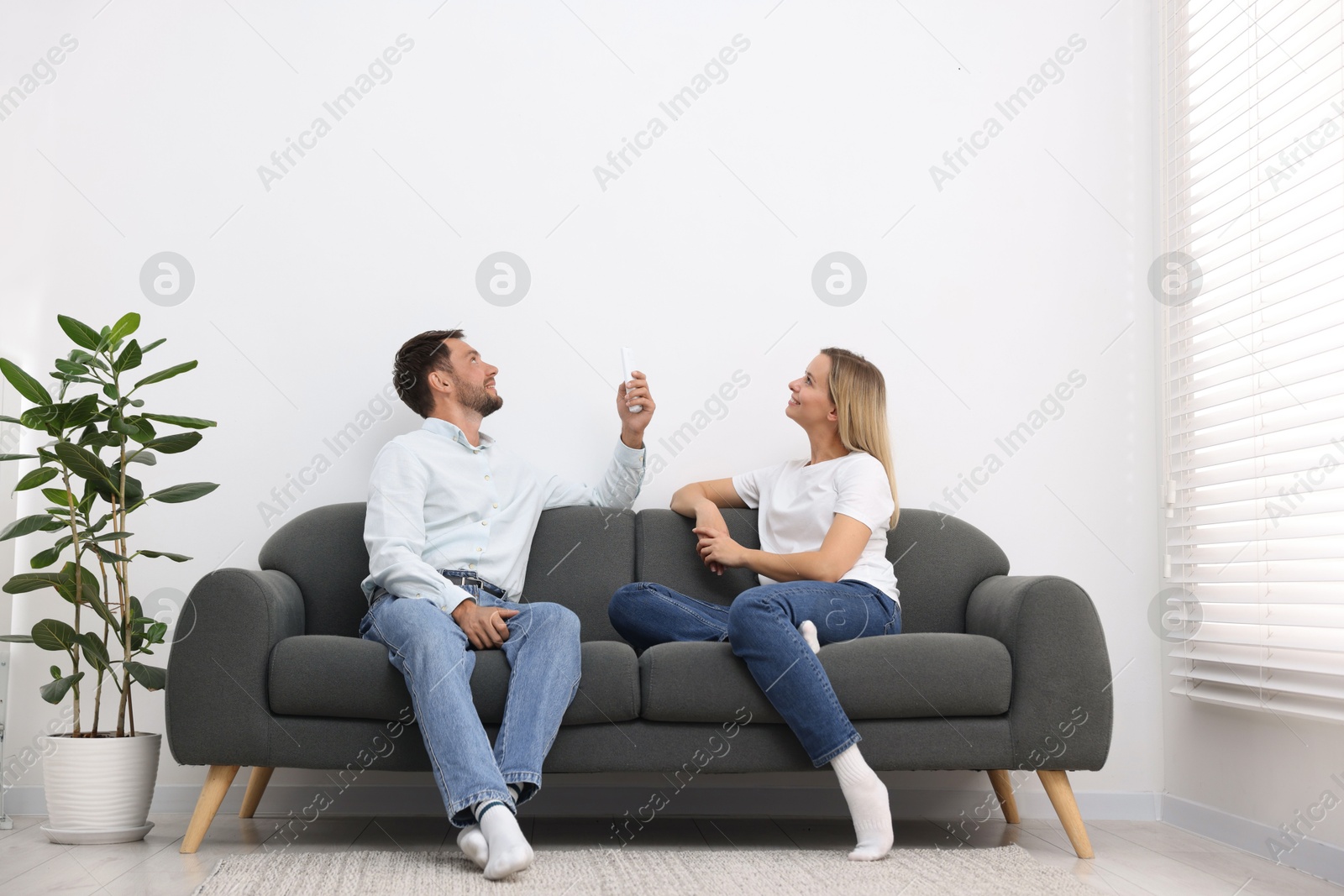 Photo of Couple using remote to control air conditioner on sofa at home