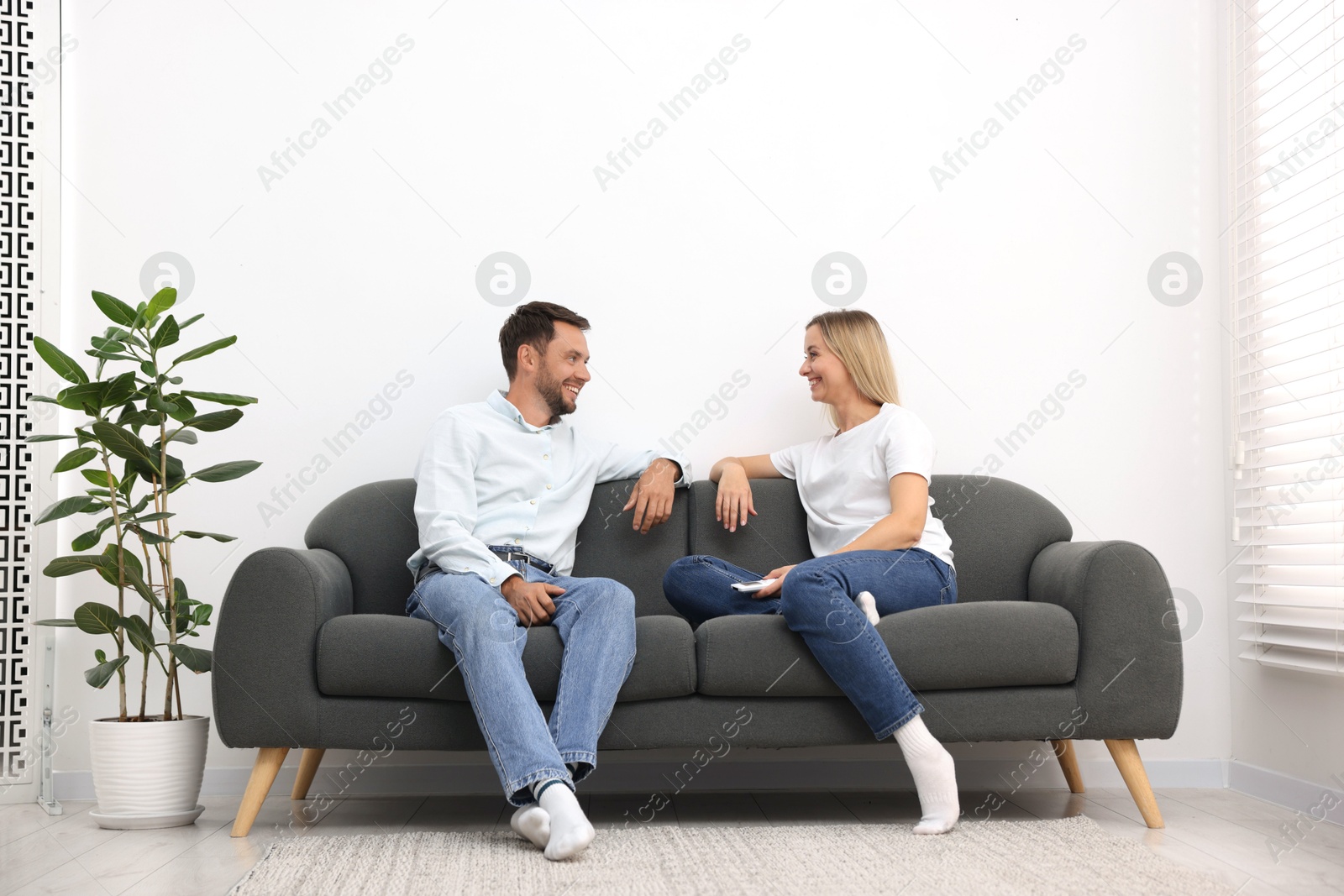 Photo of Couple with air conditioner remote control on sofa at home