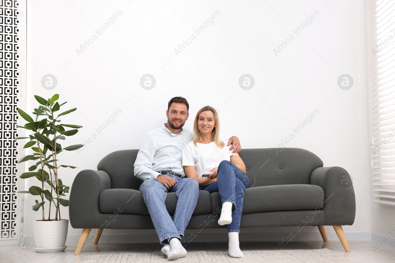 Photo of Couple with air conditioner remote control on sofa at home